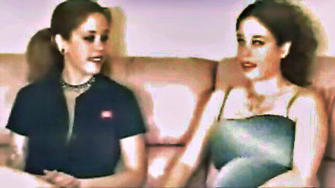 Two brunette women in casual tops chatting intimately on couch