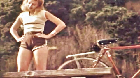 Vintage blonde in striped top and short shorts posing seductively by bike