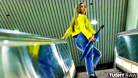 Lena Paul teases in yellow jacket and tight jeans on escalator with umbrella
