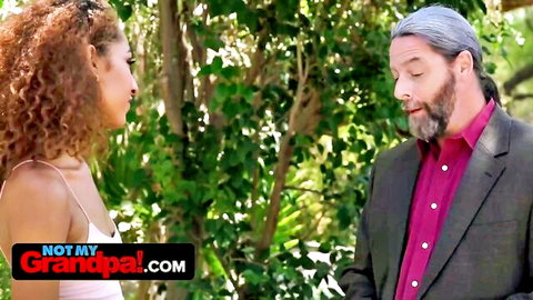 Petite redhead teen in white top chats with mature gray-haired grandpa outdoors