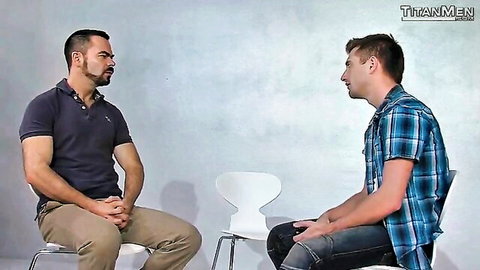 Muscular mature DILF with goatee and athletic young stud in plaid shirt sit facing each other intimately