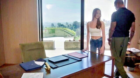 Skinny blonde teen in tight shorts smiles as muscular black guy stands close behind her in luxury office