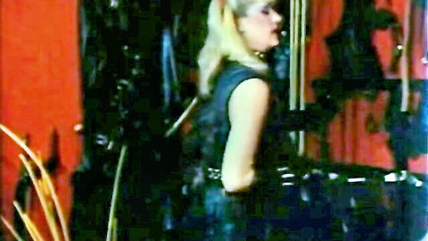 Blonde mature woman in tight black leather corset poses seductively from behind in BDSM dungeon mirror