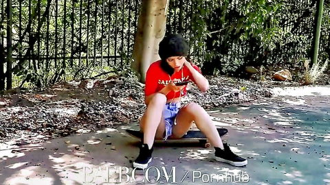 Petite brunette babe in tiny shorts sitting spread-legged on skateboard outdoors teasing