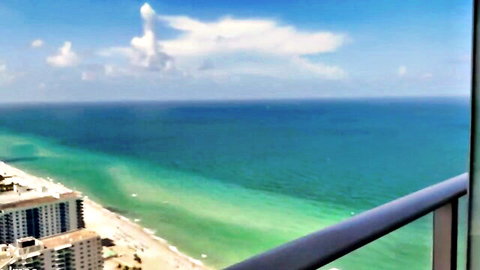 Stunning high balcony view of turquoise ocean beach and Miami high-rises on sunny day