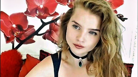 Blonde teen beauty in black choker necklace pouts seductively with wavy hair amid red orchids