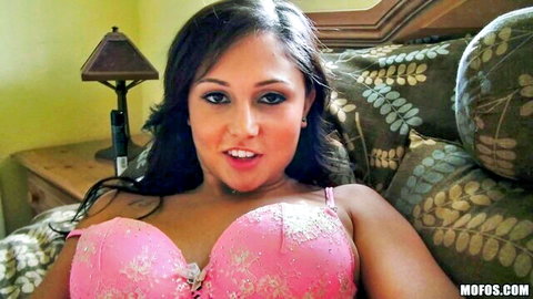 Busty brunette in pink lace bra smiles seductively showing massive cleavage on couch