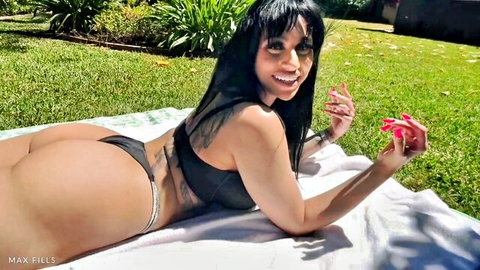 Curvy ebony babe with huge ass and big tits lying sideways in tiny black thong bikini outdoors smiling seductively