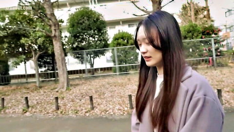 Young Asian woman with long dark hair in gray coat, shy outdoor pose, innocent look