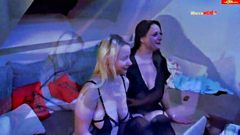 Sexy-Elli in black lingerie exposing breasts with brunette friend on couch