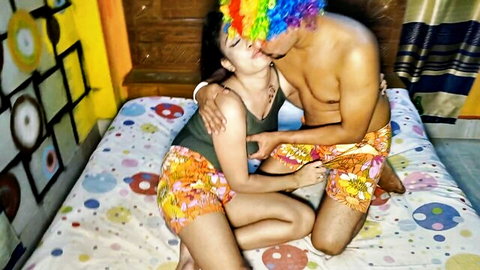 Brunette Indian babe passionately kissing shirtless guy in rainbow clown wig on bed