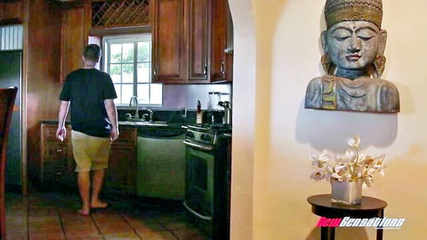 Barefoot man in black tee and shorts walks toward kitchen sink with Buddha statue on wall