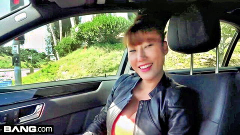 Sexy smiling Asian blonde in open leather jacket flashing cleavage from car POV