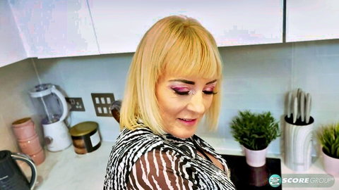 Busty blonde MILF smiles seductively in sheer striped top revealing big tits in kitchen