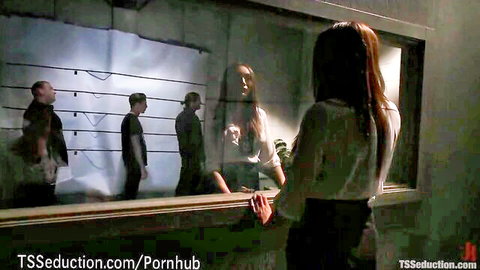 Long-haired brunette in skirt and heels faces three prisoners behind one-way mirror in TS prison tease
