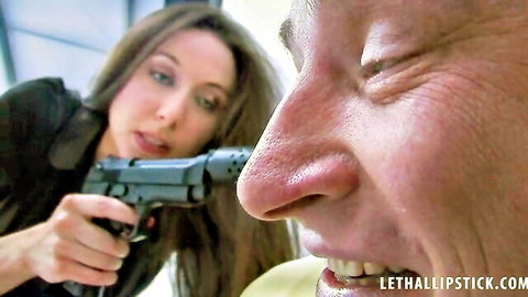 Sexy babe in black suit holds gun barrel to older man's nose and lips threateningly