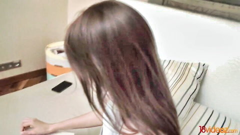 Long-haired brunette babe in white tank top teasing from behind at desk
