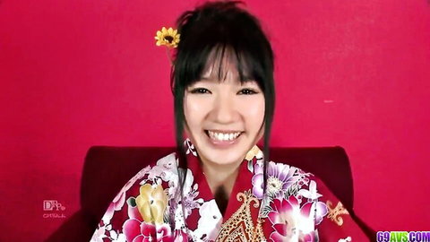Smiling Japanese babe in floral kimono teasing seductively on red sofa