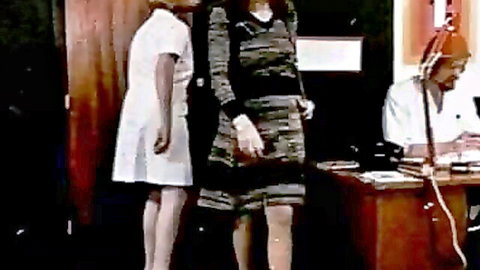 Vintage nurses in short white dress and striped top standing by doctor at desk in medical office