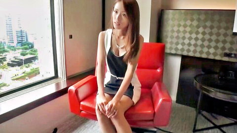 Skinny Asian babe in tight black dress teasing legs crossed on red chair in hotel room