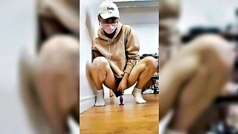 Skinny masked girl in hoodie squats spreading legs reaching for purple butt plug anal toy