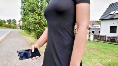 Brunette babe in tight black dress flaunting big tits outdoors holding phone