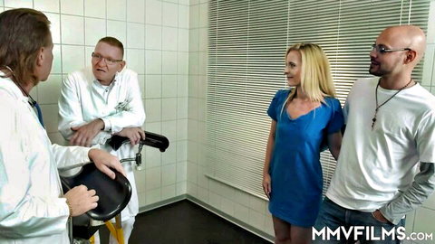 Petite blonde babe in short blue dress surrounded by two doctors and bald stud in medical clinic