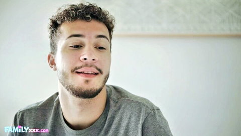 Handsome curly-haired young man smiling seductively in gray t-shirt on pinklabel.tv