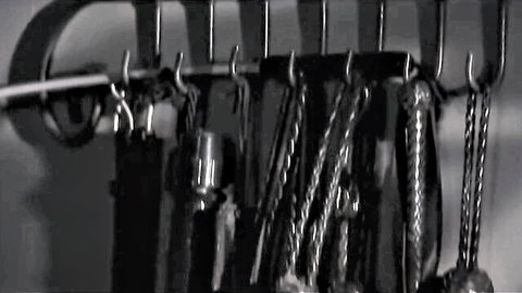 Black and white image of kitchen utensils hanging on a wall rack