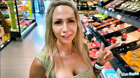 Blonde with big tits in low-cut polka dot top smiles and points at fruits in supermarket