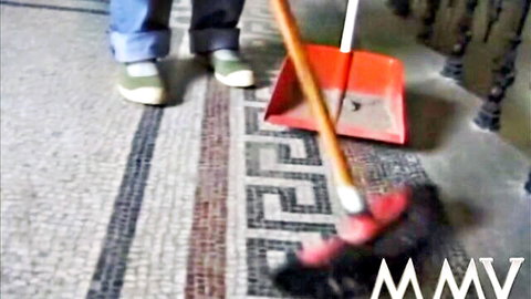 Woman's legs in rolled jeans and green sneakers sweeping mosaic floor with broom and dustpan