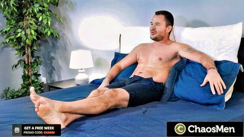 Muscular tattooed hairy stud lounges shirtless in shorts teasing on bed solo