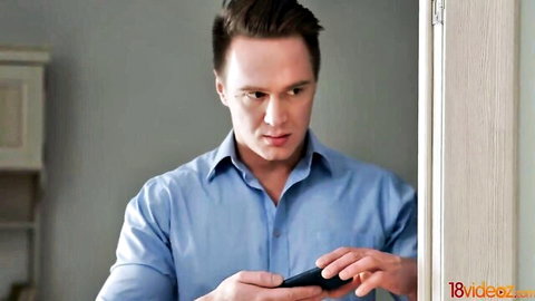 Handsome man in blue shirt holding phone intently in modern kitchen
