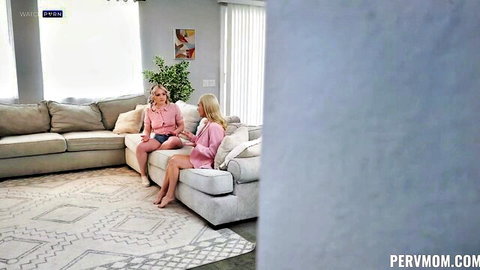 Blonde stepmom and stepsister in short skirts sitting crossed-legged on couch teasing