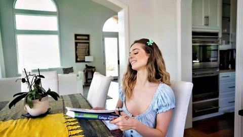 Molly Little in low-cut blue dress, smiling with cleavage tease while reading