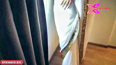 Indian woman in white saree teasing by hotel window with hand on curtain
