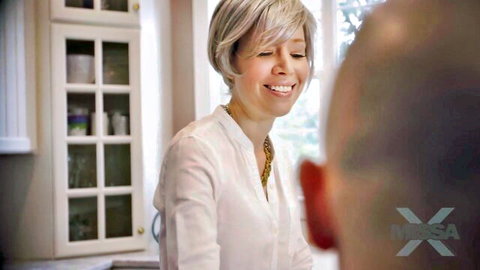 Smiling short-haired blonde MILF in white blouse flirts with bald man in kitchen