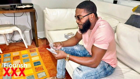 Handsome black stud in pink shirt counting thick stacks of cash on couch