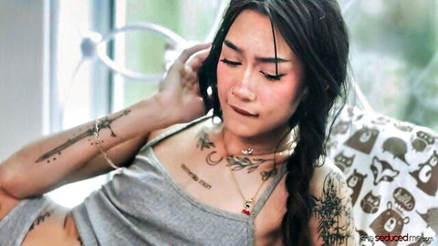 Tattooed skinny Asian beauty with small tits lounging seductively in gray tank top showing cleavage