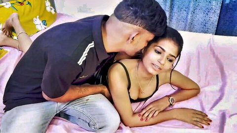 Indian man passionately kisses South Asian woman's neck while she lies in black bra showing cleavage on bed