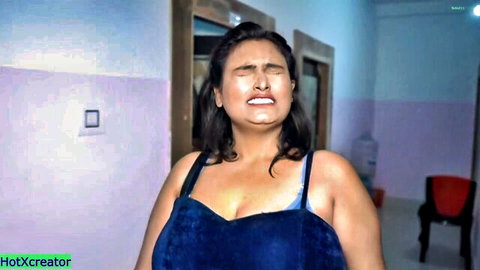 Curvy Indian woman in tight blue top grimacing in ecstasy with deep cleavage exposed