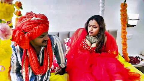 Indian bride in red saree holds groom's hand romantically on wedding bed