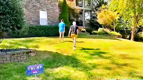 Two men in shorts walking away on grassy lawn near Trump campaign sign