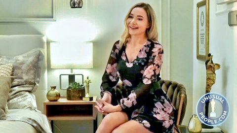 Smiling blonde in sheer floral dress sitting seductively in luxurious bedroom