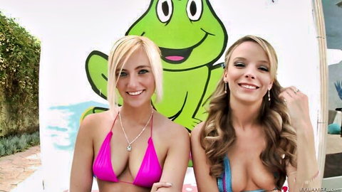 Two smiling busty blondes in skimpy bikinis flaunt cleavage next to giant green frog