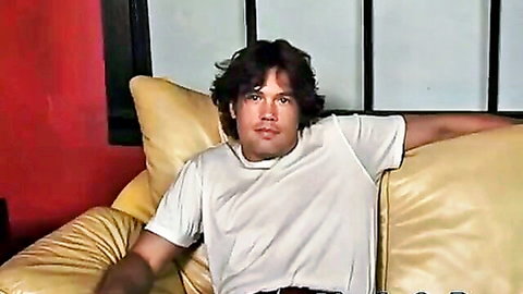 Hot curly-haired white guy lounging seductively in white tee, ready for gay action