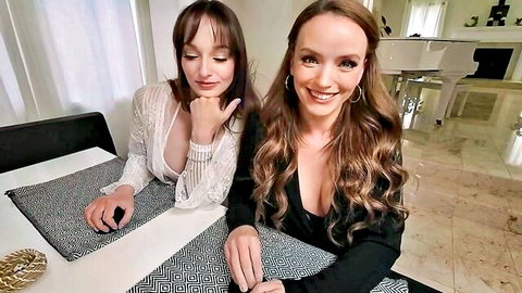 Two busty brunette MILFs in deep cleavage tops smiling seductively at POV camera on table
