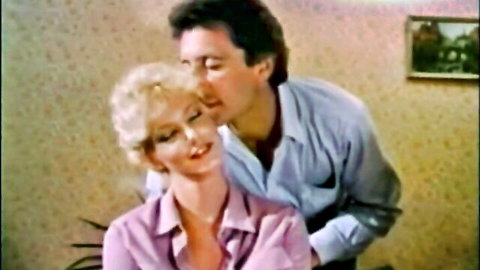 Vintage VCA couple scene: blonde woman in pink blouse kissed on neck by man