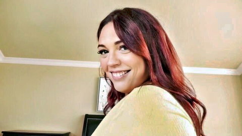 Smiling redhead babe with long wavy hair in loose yellow top teasing in bedroom