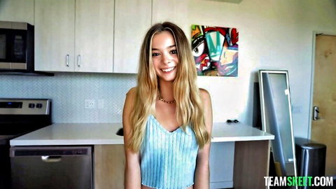 Petite blonde teen smiles teasingly in tight light blue tank top showing small tits in kitchen